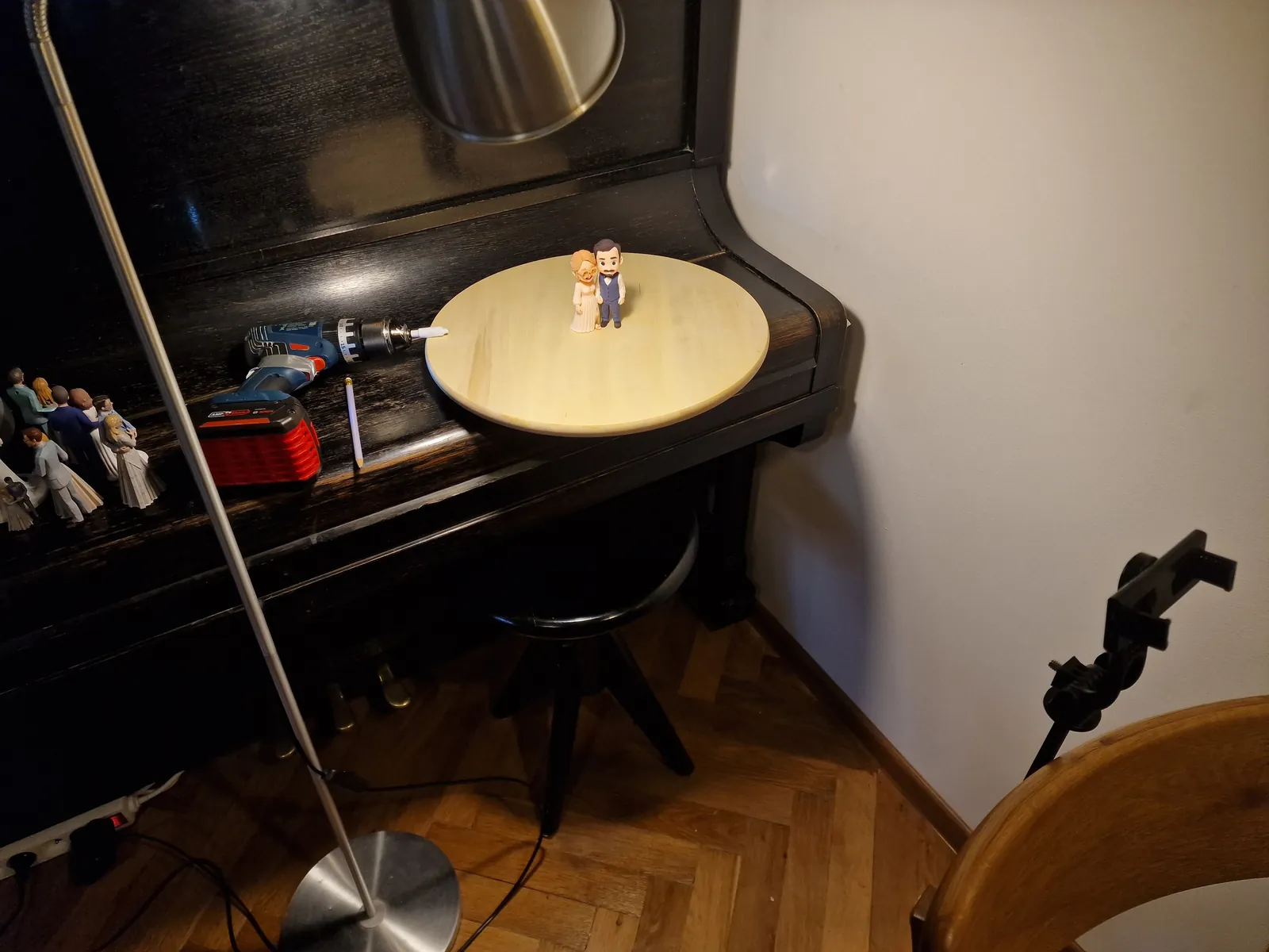 A wooden disc held in a cordless drill on a piano lid, a topper standing on it, one lamp on a stand and a phone clamped opposite